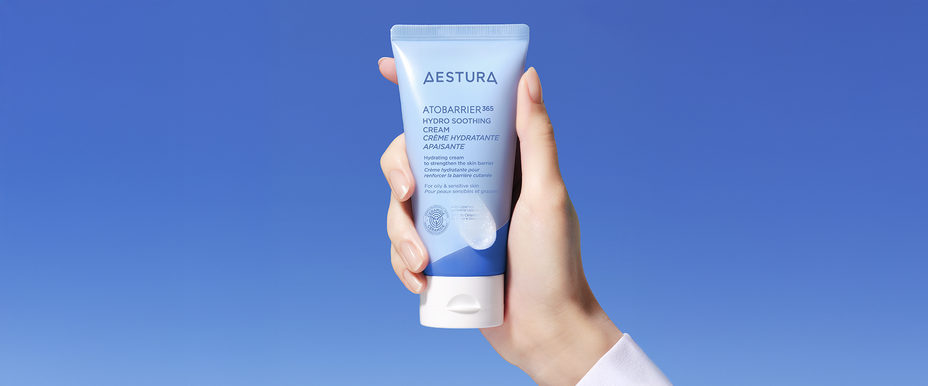 Hand holding Aestura Atobarrier365 Cream in front of a solid blue background