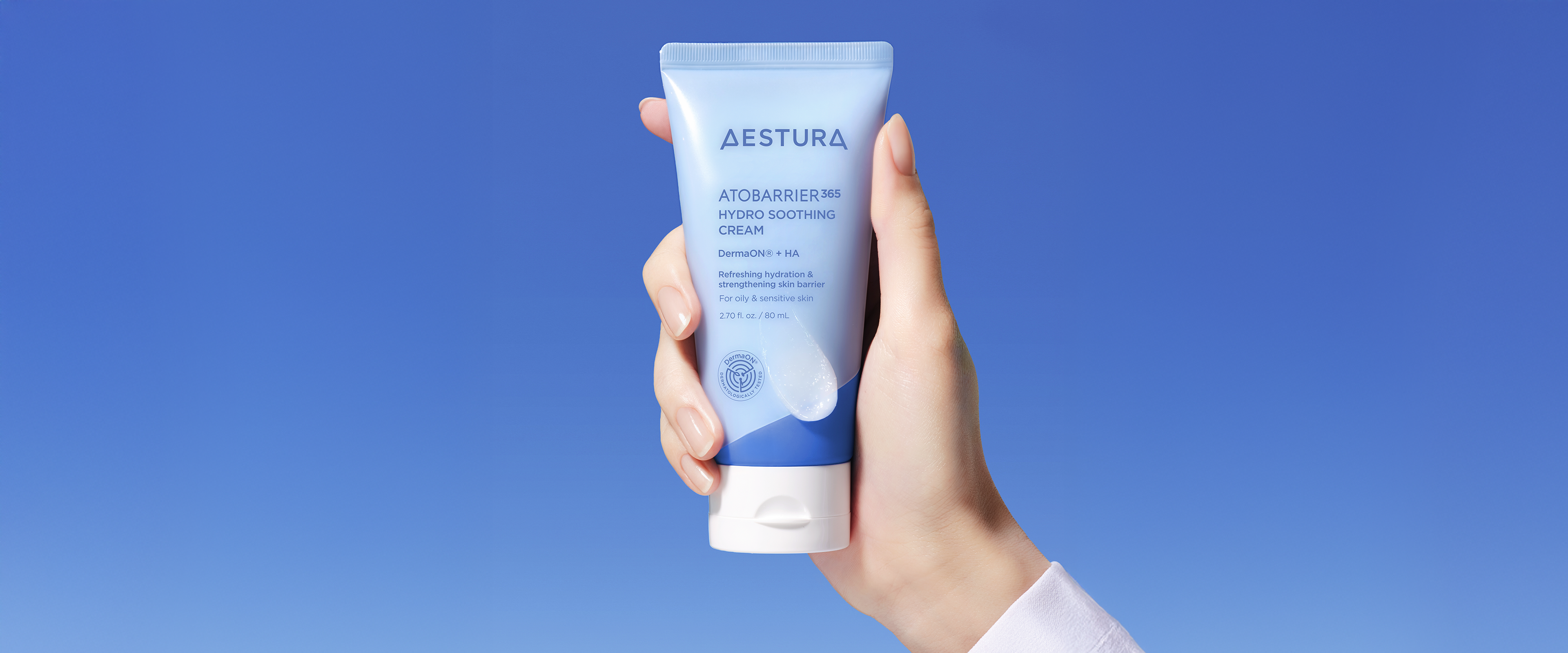 Hand holding Aestura Atobarrier365 Cream in front of a solid blue background