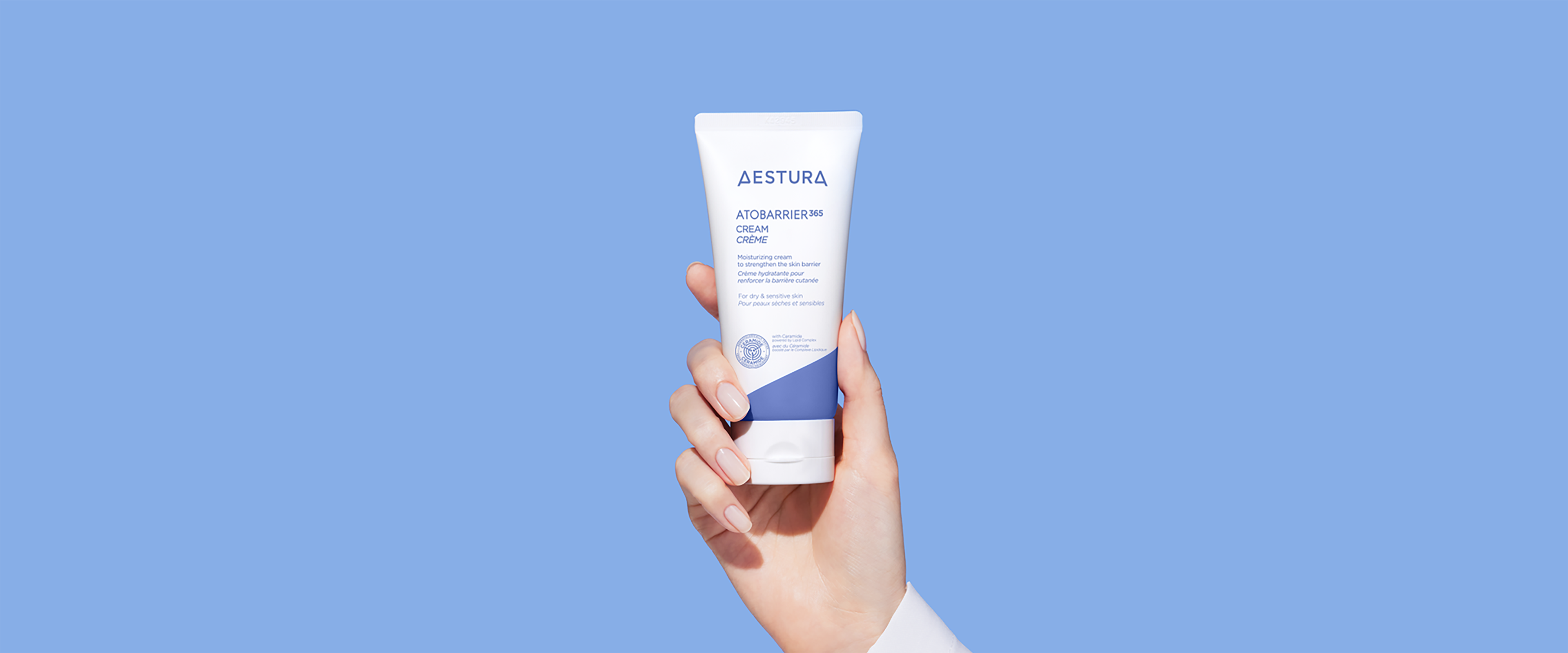 Hand holding Aestura Atobarrier365 Cream in front of a solid blue background