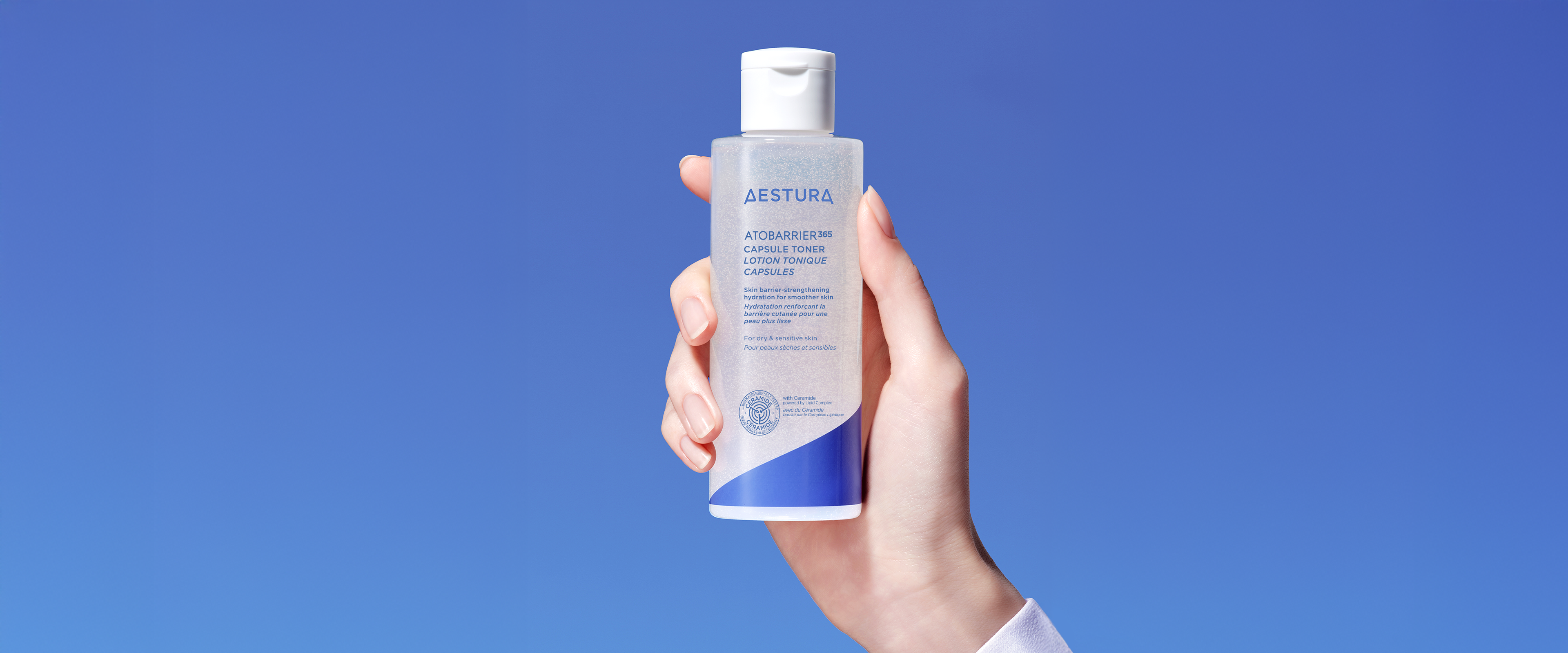 Hand holding Aestura Atobarrier365 Toner in front of a solid blue background